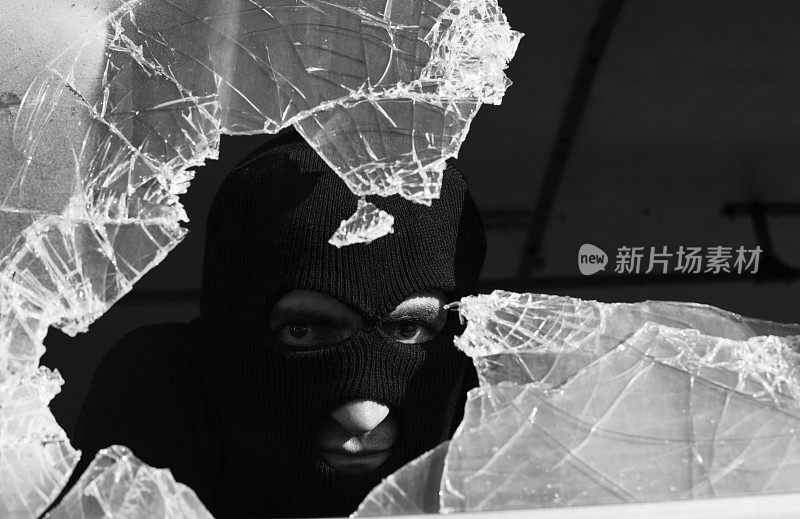 一个成年男子戴着面罩从碎玻璃后面偷窥