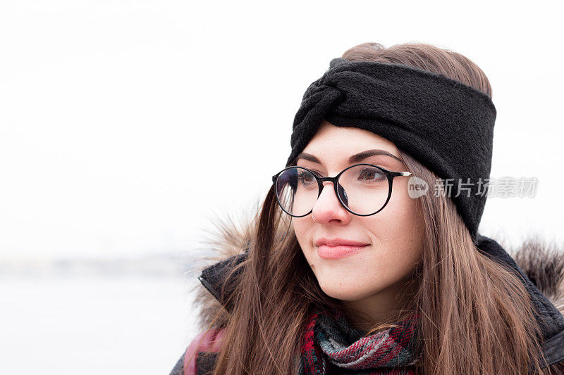 女孩在冬天的衣服，眼镜和温暖的针织头带。一个年轻漂亮的女人的肖像。自然的背景。户外。