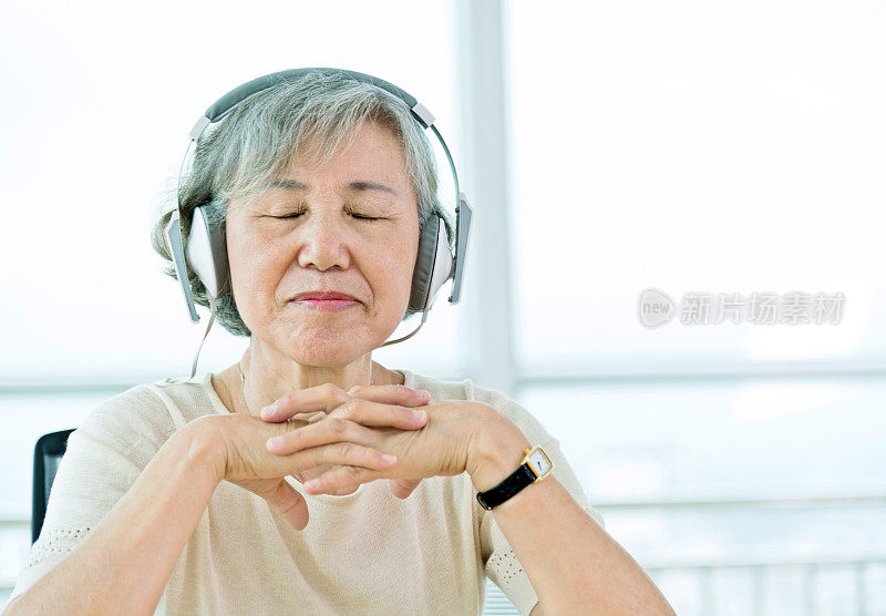 一位年长的亚洲女性正戴着耳机听音乐