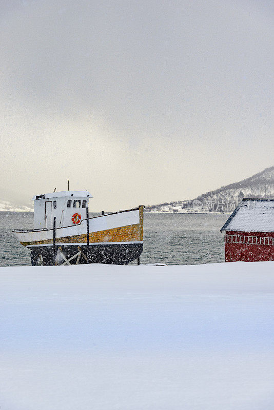 冬天，挪威北部峡湾岸边的一艘挪威渔船和棚屋。