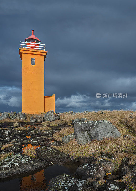 橙色灯塔在冰岛海岸线的岩石池上反射