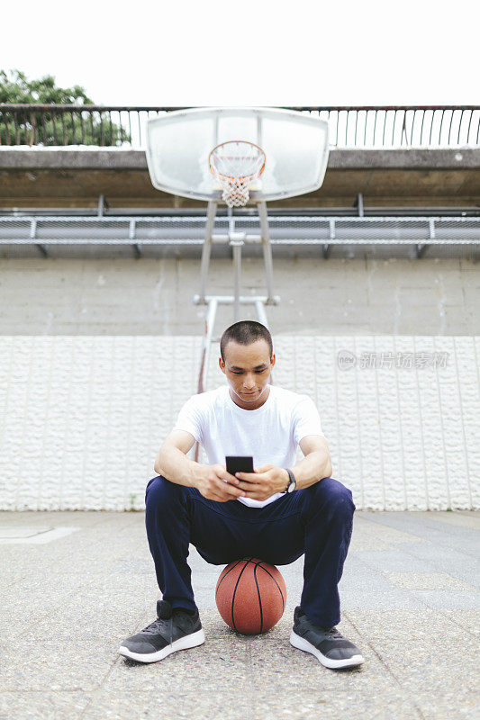 年轻的日本男子坐在篮球和使用智能手机