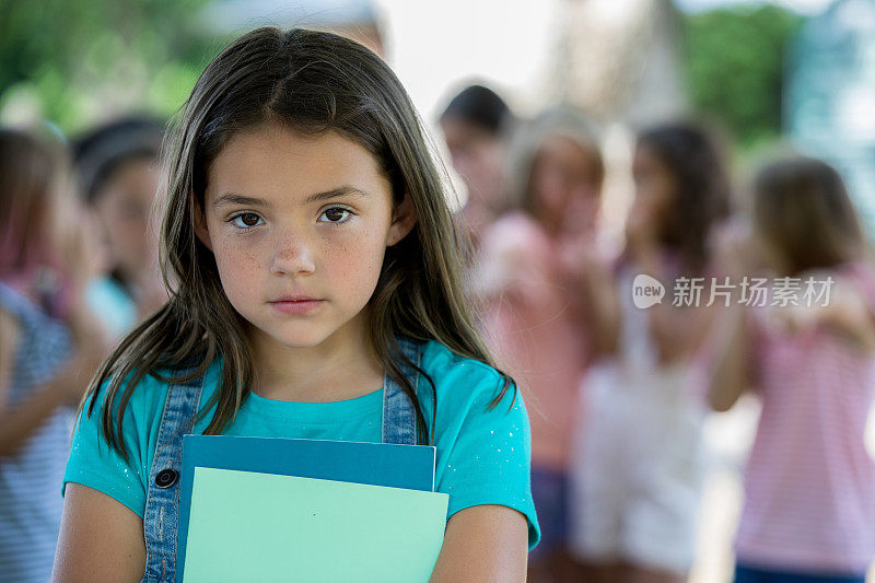 沮丧的小女孩盯着相机，同学们在后面欺负她