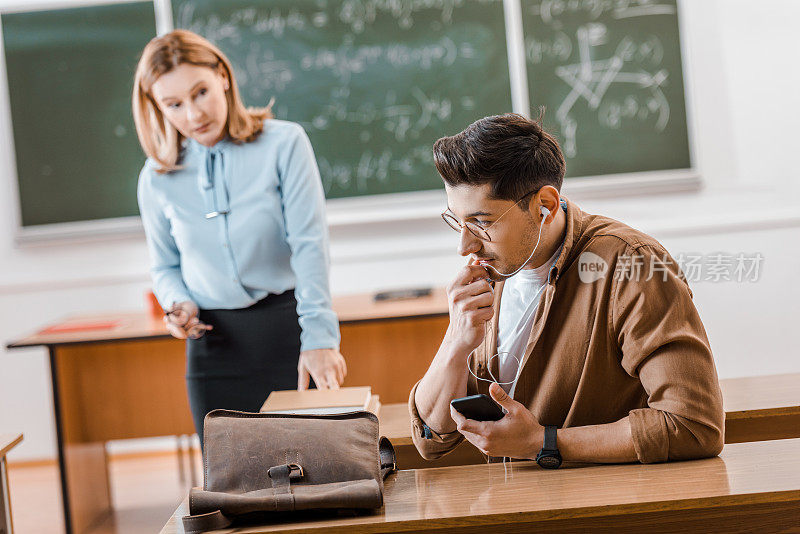 学生戴眼镜，戴耳机，在教室里用智能手机讲话