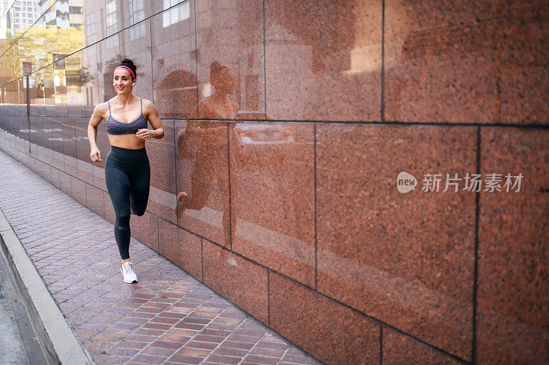 活跃的女性穿着运动服，戴着无线耳机在市中心的街道上慢跑