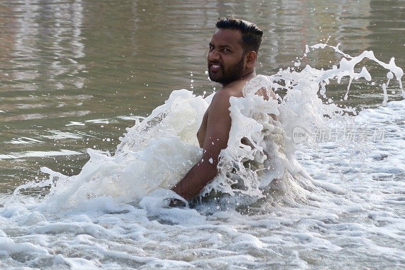 赤裸胸部的印度男子练习莲花姿势(莲花瑜伽)瑜伽位置在潮湿的沙滩上，水的边缘，帕洛伦海滩，果阿，印度