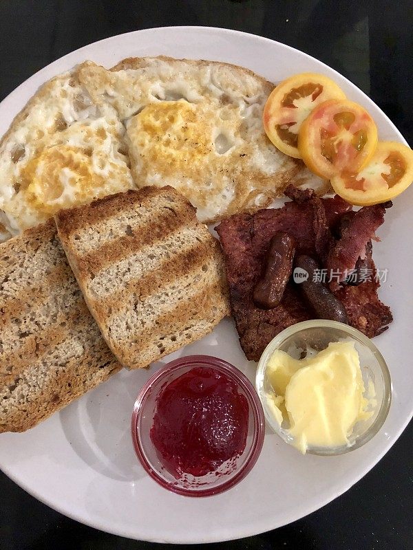 外国版本的全英式早餐在假日油炸，鸡尾酒香肠，煎火腿培根，两面煎蛋，西红柿片，棕色吐司与全麦果酱和黄油