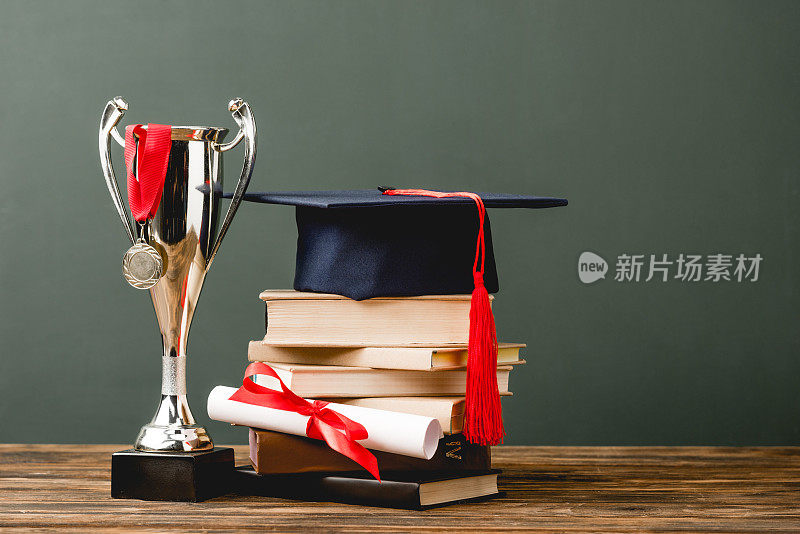 书籍，文凭，学位帽，奖杯和奖章在木制表面孤立在灰色