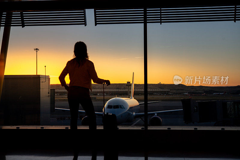 日出时，一名成年女子透过窗户看机场