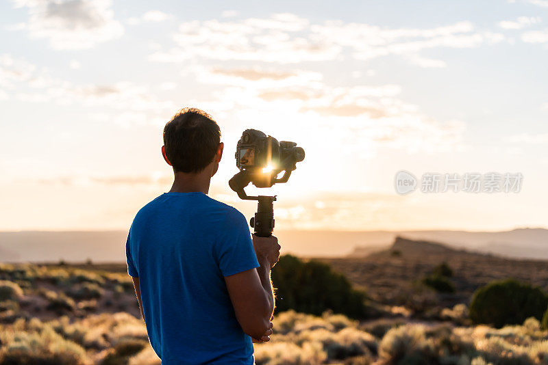 在犹他州拱门国家公园，手持万向节摄像机稳定器的人通过设备拍摄日出与日射耀斑，在炽热的火炉视点