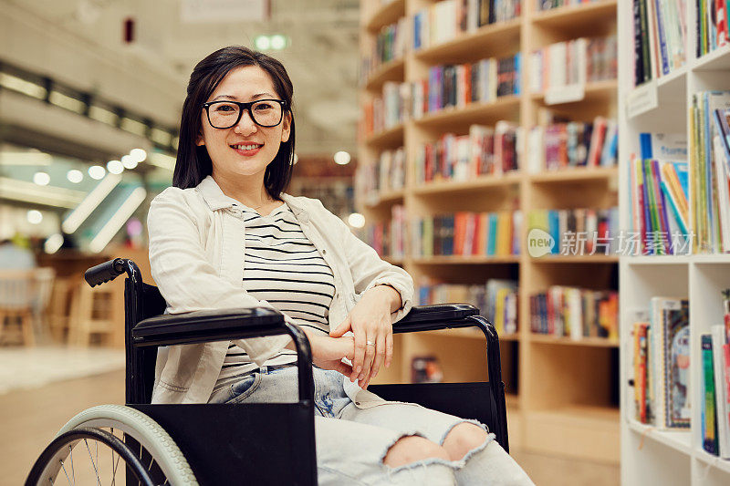 肖像快乐的黑发亚洲学生女孩戴眼镜使用轮椅在大学图书馆的交通工具