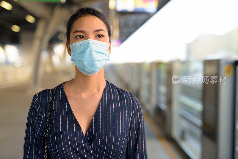 年轻的亚洲女商人戴着口罩在轻轨站等待预防冠状病毒爆发