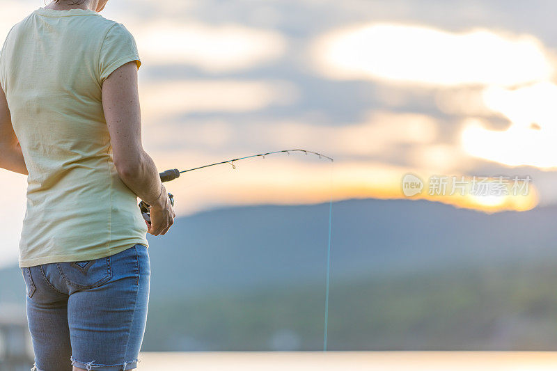 一个年轻的女人在夏天的日落钓鱼