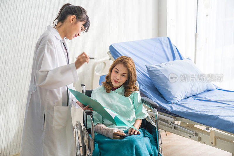 在医院里，坐在轮椅上的病人，专业的医生在为女性折叠的骨折手臂和包扎的手解读x光图像