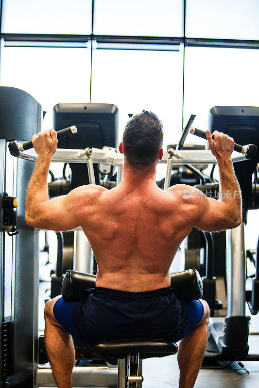赤裸上身，肌肉发达的男性运动员在健身房用肩膀按压