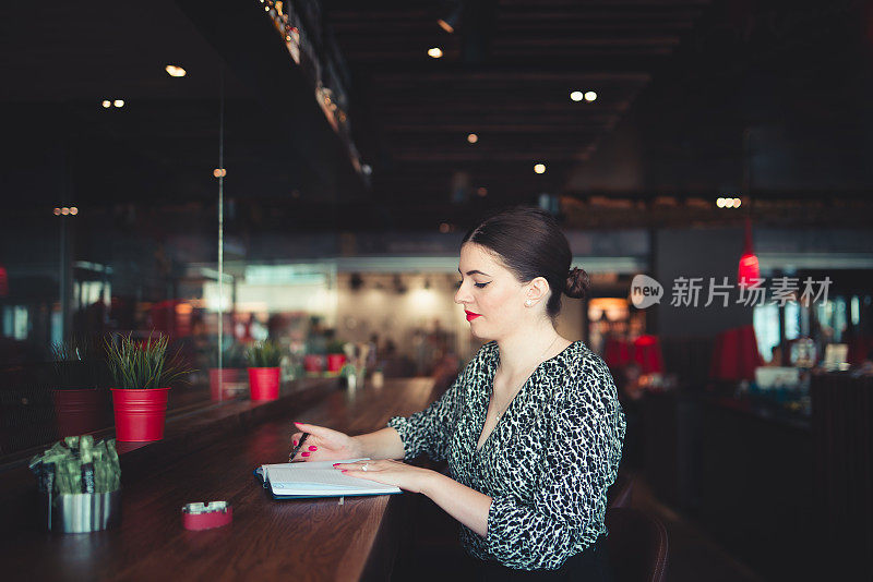 盘算着下一步的行动计划，一个女商人在咖啡店写笔记的特写镜头。