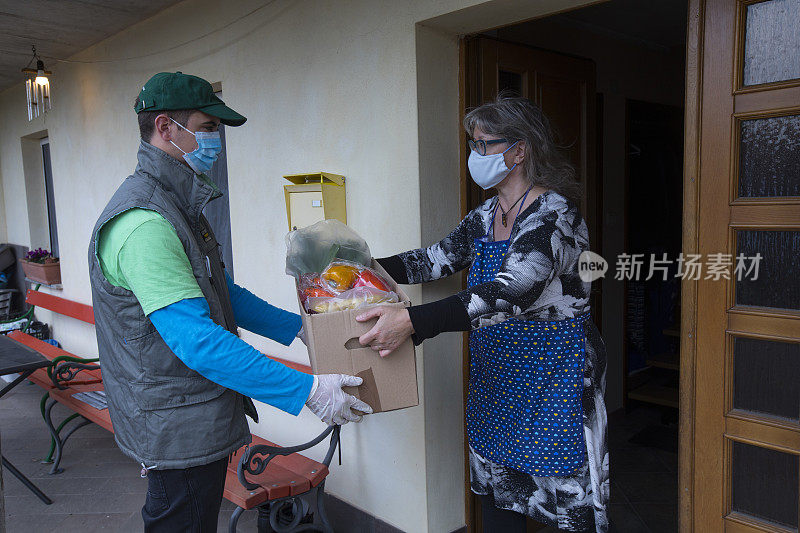 在冠状病毒隔离期间，一名送货员早晨将食品杂货送到一名成年妇女的家门口