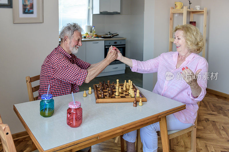 微笑的老夫妇在家里放松和下棋。