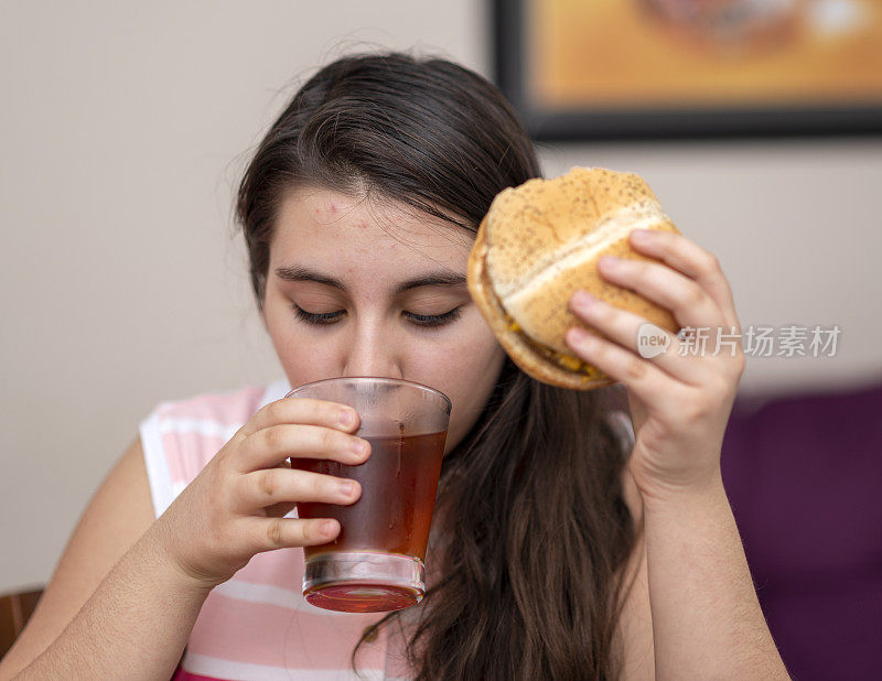少女在屋里吃汉堡，喝冰茶