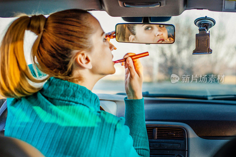 年轻优雅的女子在化妆时看着汽车视镜