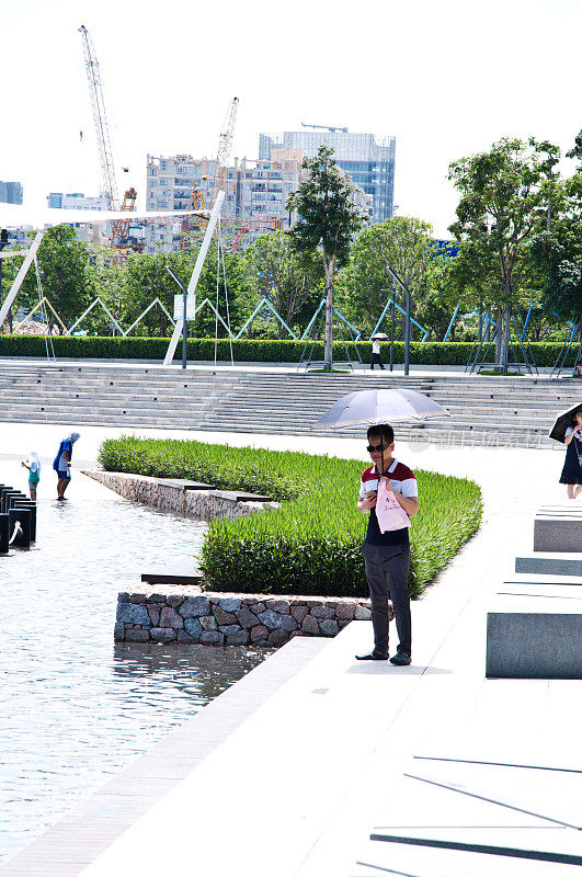 中国深圳，一名男子在深圳人才园撑伞躲避烈日。这个公共主题公园与深圳湾公园和湾体育馆相连