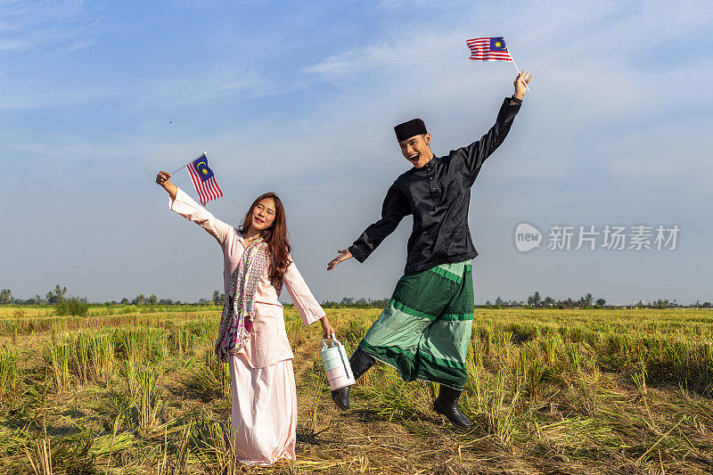 莫迪卡，快乐的马来西亚男人和女人男人拿着国旗在稻田里跳跃