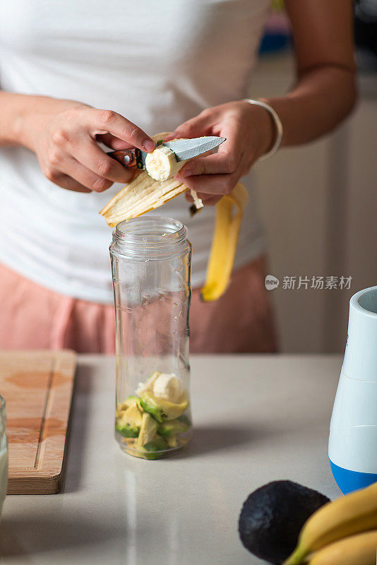 一个女人正在切香蕉，准备做鳄梨和香蕉冰沙作为健康的早餐饮料