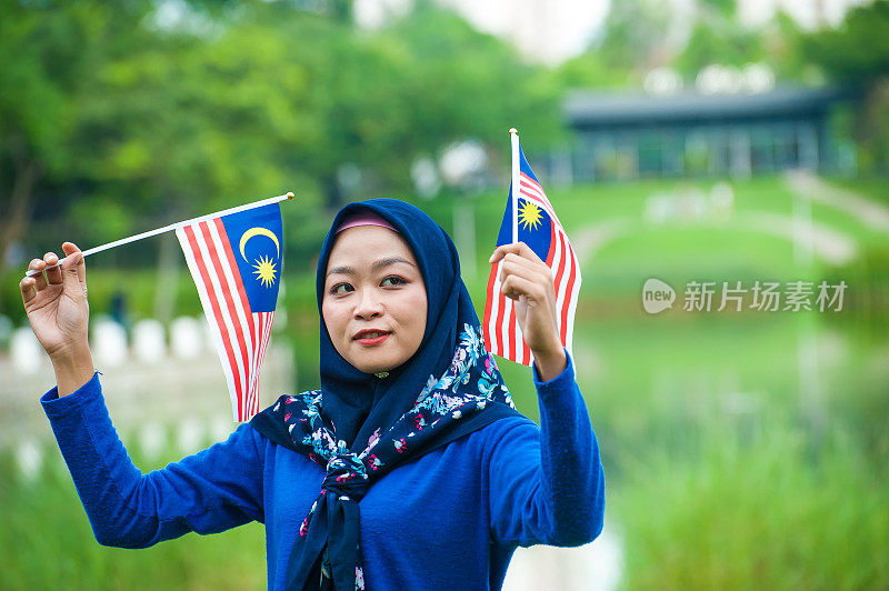 年轻的马来西亚妇女挥舞着马来西亚国旗，带着崇高的爱国主义精神庆祝独立日
