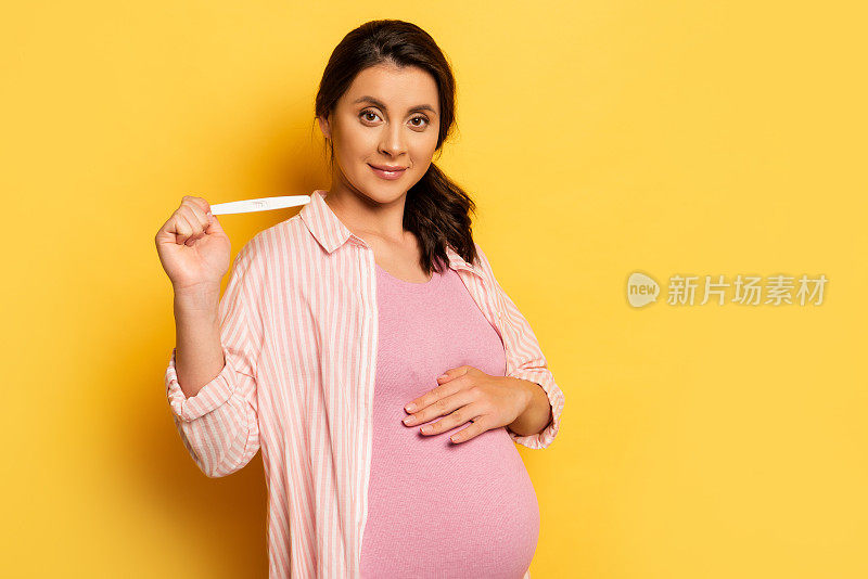 孕妇摸着肚子，验孕试纸显示黄色