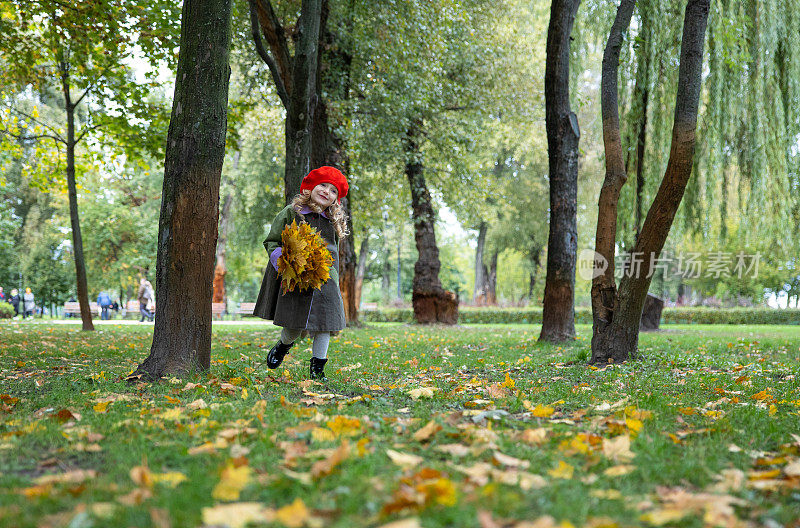 快乐的小女孩带着黄色的枫叶在公园里奔跑。