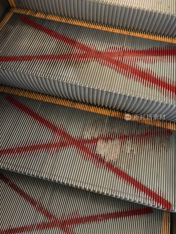 自动扶梯上的金属台阶特写，上面画着巨大的红色喷漆十字，关于移动楼梯台阶的新冠肺炎社交距离规定，新冠肺炎安全
