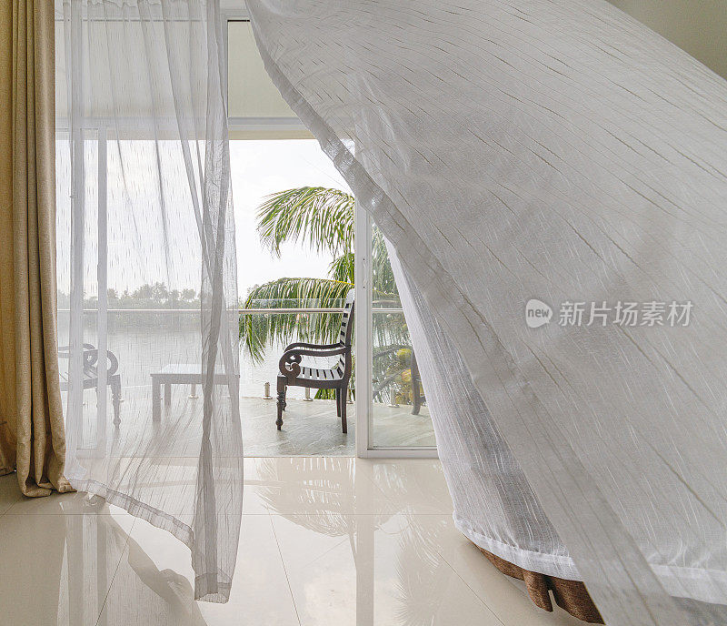 风吹动着敞开的阳台窗户上的窗帘，从现代化的空酒店房间可以看到河上的风景。