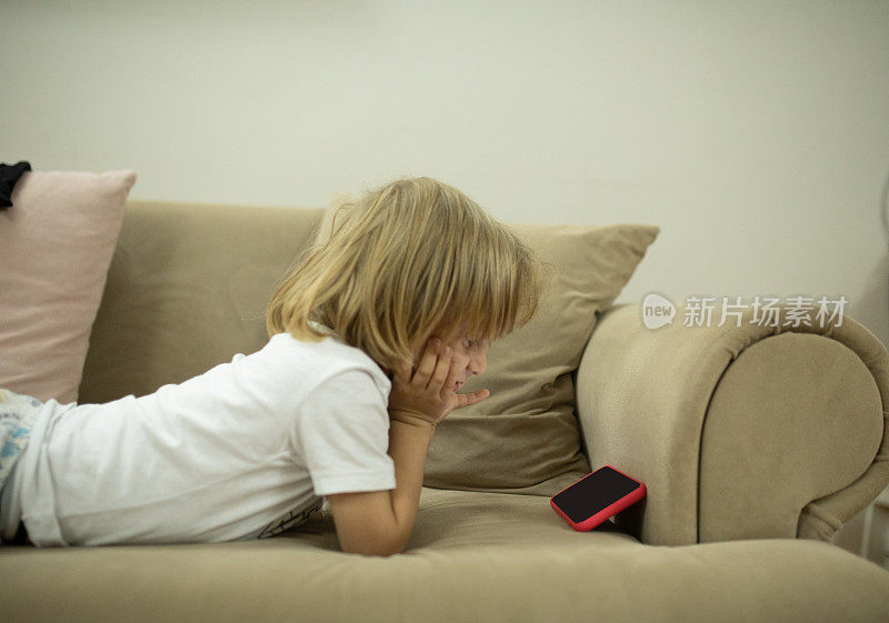 男孩在沙发上用智能手机看视频
