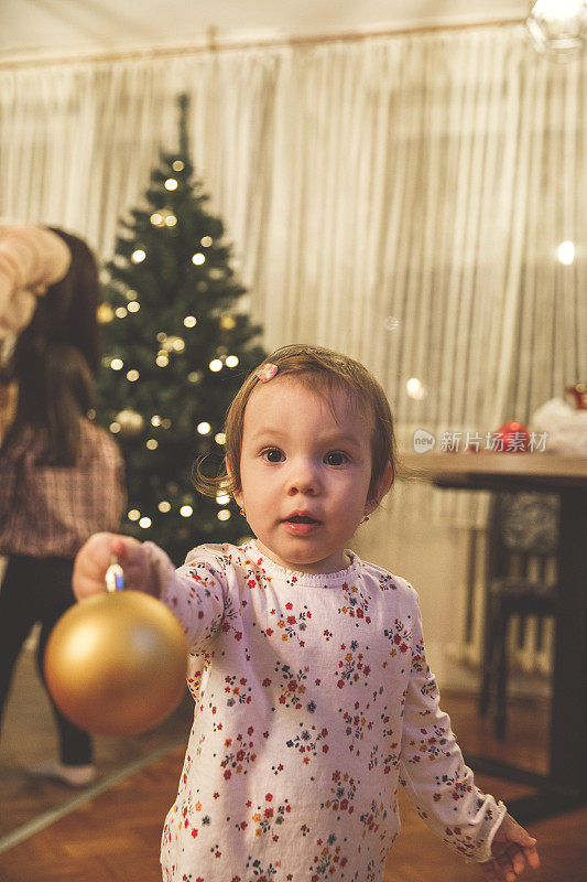 小女孩给相机一个金色的圣诞装饰品