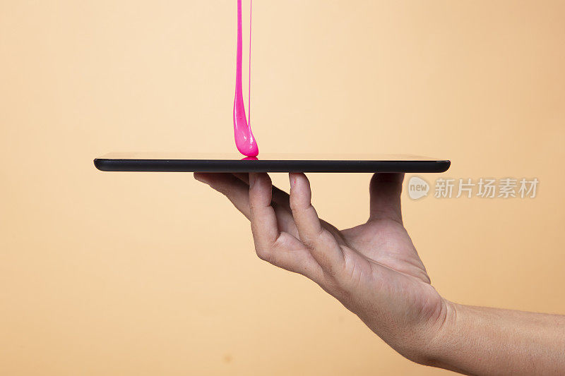 女人的手使用数字平板电脑与霓虹粉色黏液玩具在橙色波普艺术背景。