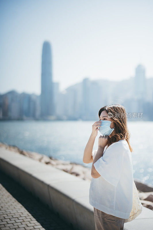 一名亚洲年轻女子戴着防护面罩，在香港的海滨长廊旁仰望天空