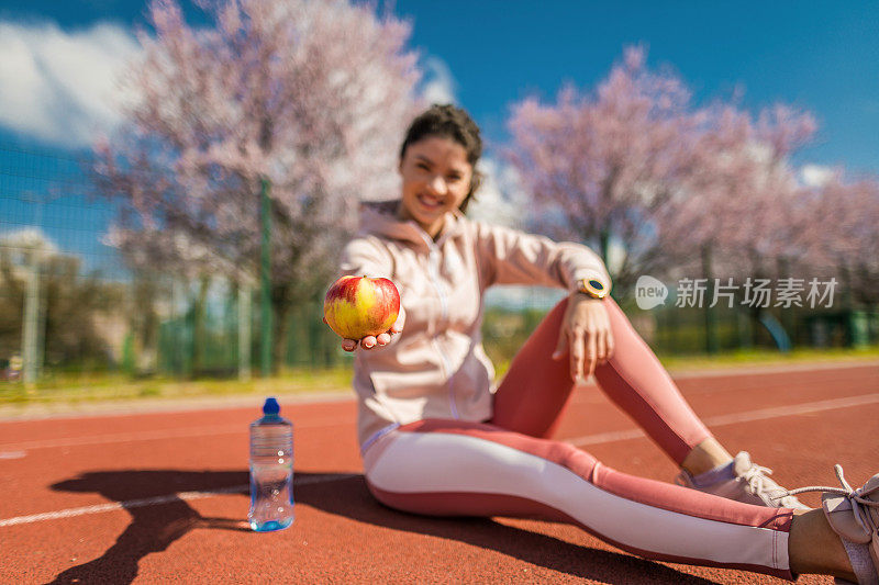 运动的年轻女子在跑道上跑步后吃苹果。