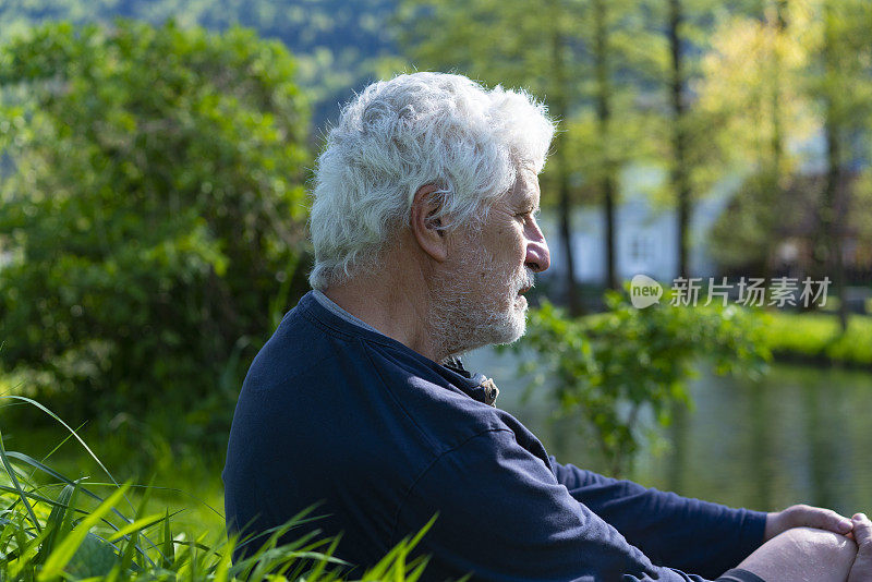 一位老年帕金森患者坐在草地上，欣赏着斯洛文尼亚Kočevje河的景色。