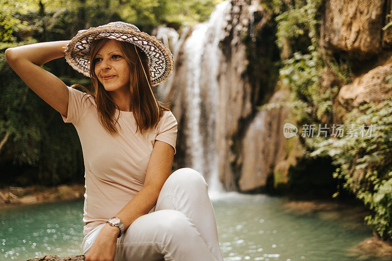 一个美丽的年轻女子，头上戴着一顶帽子，坐在瀑布旁边