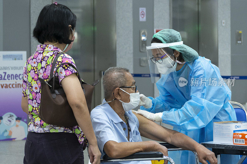 在方苏大车站，一名亚洲医生或护士正在给戴着冠状病毒防护口罩的老年男性患者注射新冠病毒疫苗。