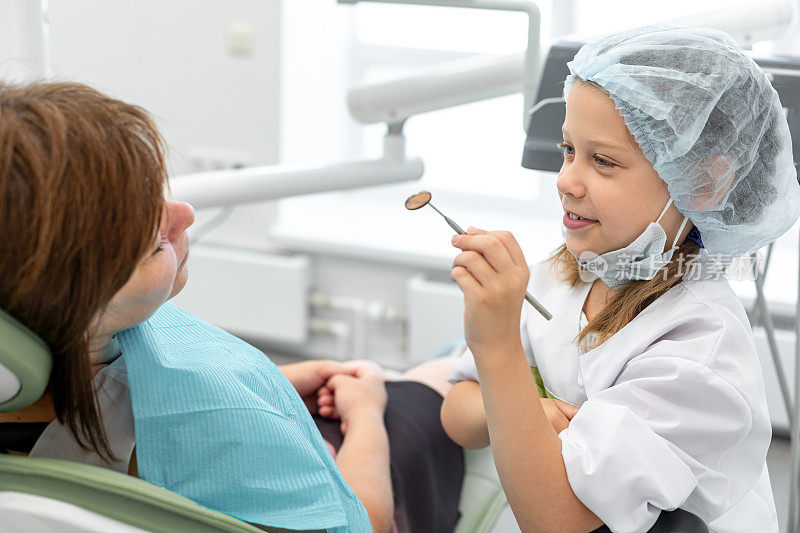 小女孩和她的女牙医互换角色。手持牙科器械的小孩，女牙医描绘病人