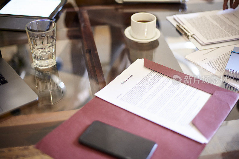 高视角的文件，智能手机，一杯咖啡和一杯水上面的玻璃桌子