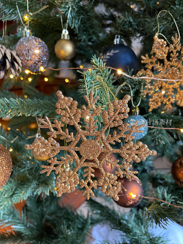 个人的特写图像，铜，闪闪发光的雪花挂在人造圣诞树的树枝上，蓝色的小饰品，云杉针，模糊的白色童话灯的背景