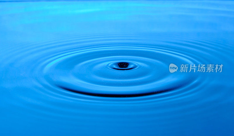 明亮的蓝色背景与发散的圆圈从水滴表面的水。