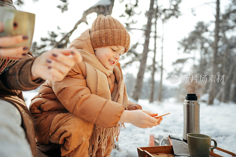 年轻女子带着儿子在冬日森林里野餐，喝着热茶