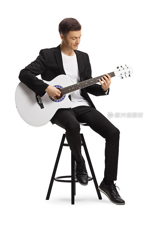 优雅的年轻人穿着黑色西装坐在椅子上，弹着白色的原声吉他