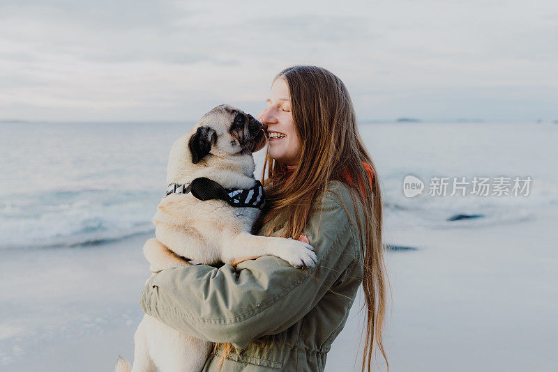一个女人在海滩上抱着一只可爱的哈巴狗，感觉爱和幸福