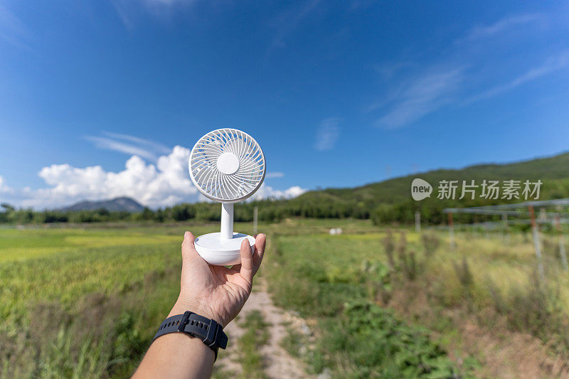 一只手拿着小塑料扇，在蓝天白云的田野里