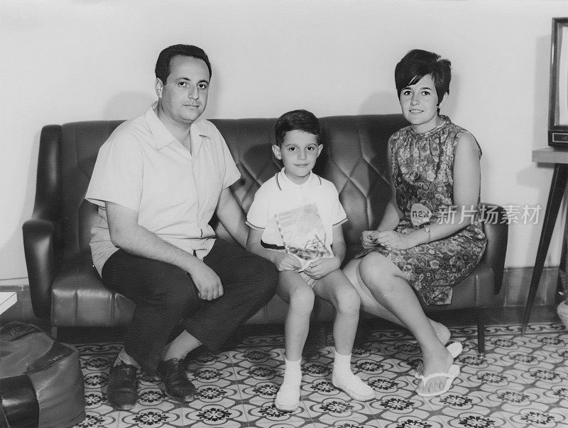黑白照片摄于60年代，一对夫妇和他们的儿子坐在客厅沙发上