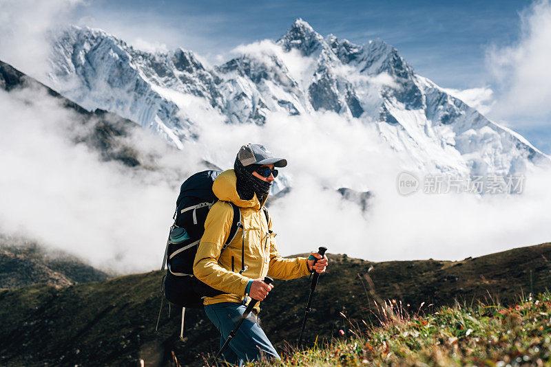 年轻人户外旅行者走在巨大的阳光多云的山路上。背着双肩包，拄着登山杖穿越山路的游客